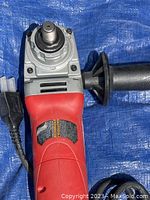 Front view of Milwaukee 5 inch angle grinder showing the head and spindle where the grinding disc attaches. Included is a side handle attached to the tool.