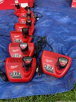 Six Milwaukee M12 chargers arranged on a blue tarp