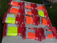 Twelve Milwaukee brand safety vests packaged individually, showing neon orange and neon yellow colors, stacked and arranged.