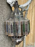 Side view of hexagonal metal frame with colored glass panels in blue, green, and red. Shows overall shape, hanging chain, and weathered metal condition.