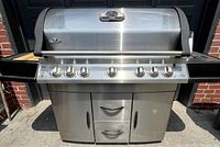Front view of closed grill on stainless cart showing control panel, knobs, and storage doors/drawers