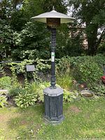 Full view of the tall outdoor propane heater standing on grass with surrounding greenery.
