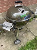 Full view of Weber charcoal kettle grill showing lid, wheels, and chimney starter on side.