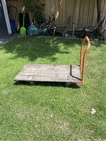 Wood and metal dolly placed on grass showing wooden platform and orange metal handle upright.