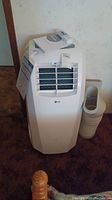 Front view of white LG portable air conditioner showing intake vents and included accessories on top