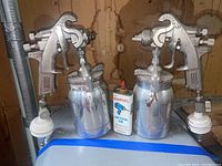 Two Sharpe Model 450 air paint sprayers with metal paint containers and a can of Marvel air-tool oil shown together on a surface.