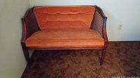 Full view of bench showing orange upholstery, cane side panels, and wood frame with slight scratches.