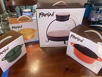 Photo showing boxed Parini ceramic casseroles and the 2-tier chip and dip set boxes on a wooden table.