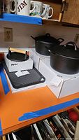 Photo showing two cast iron Dutch ovens with lids and the Parini burger press on its box next to the cast iron grill plate.