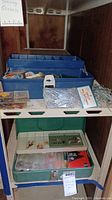 Blue plastic tackle box on shelf with fishing accessories inside; spools of line and packaged bobbers visible