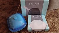 Two boxed Belfer cookware items with blue ceramic lidded casserole placed outside boxes on floor.