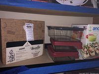 Overview photo showing boxed Appétit Marseille stoneware casserole next to stacked glass storage containers with red lids.