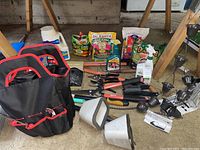 Lot including gardening tool bag, hedge trimmers, fertilizers, rain chain cups and spigot covers laid out on floor