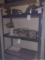 Metal shelving unit with wooden shelves holding various home items. Metal frame is dark with wood shelves. Shelf measuring tags attached.