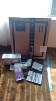 Box containing Bissell handheld cordless vacuum, blood pressure monitor, and other items arranged on carpet.