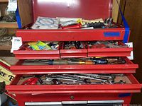 Opened drawers of red tool chest showing assorted hand tools including wrenches, screwdrivers, and hardware items.
