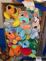 Top view of assorted TY Pillow Pals plush toys inside a cardboard box showing a variety of bright colors and animal shapes.