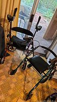 Photo showing two walkers, one red with attached arm crutches and one green with a padded seat, inside a room near a sliding glass door.
