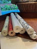 Six large wallpaper rolls from end view showing varied colors and patterns.