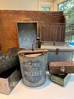 Photo showing the full assortment of antique Acme ice cream freezer bucket and various metal boxes and baskets arranged on a table with wooden backdrop.
