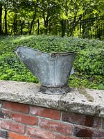 Side profile view of the antique metal coal bucket showing the wide spout and weathered galvanized metal surface with rust marks.