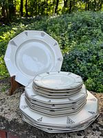 Stacked view of 12 octagonal art deco china plates arranged in three groups by size with silver geometric designs around rim.