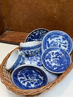 Close-up of four Blue Willow patterned plates and two teacups in a wicker basket