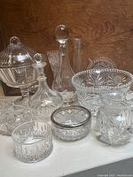 Photo showing large bowl, decanter, covered compote, and assorted smaller crystal and glass items on a white surface against a wooden background
