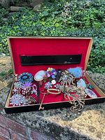 View of the vintage red-lined jewelry case with assorted vintage costume jewelry inside including earrings, brooches, and pins.