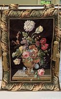 Front view of the floral wall tapestry hanging on the included rod with tassels, showing detailed flower arrangement in vase and decorative border.