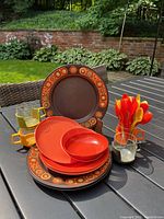 Photo showing the full set of Melmac dishes, stacking cups, and colorful spoons arranged outdoors on a patio table with garden background.