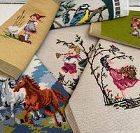 Photo showing six finished needlepoint pieces partially overlapping. Designs include a brown horse running, children playing instruments, a girl holding flowers, birds on branches.