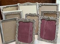 Full view of nine pewter picture frames showing a variety of floral and bird decorative motifs in different sizes and designs