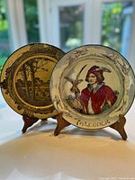 Both Royal Doulton plates displayed on table with wooden stands, showing front detailed designs.