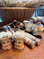 Vintage ceramic salt and pepper shakers shaped as chef heads, ceramic chef figurines, and rolled wallpaper borders in front of a woven basket.