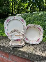 Image of the full set including large square dinner plate, medium round plate, small round plates, gravy boat with underplate, and square bowls, all decorated with pink rose floral patterns and gold trim.