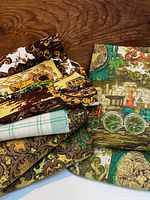 Photo of folded vintage fabrics showing a fabric with covered wagon print, a green and white plaid fabric, a damask patterned fabric, and a vintage train print fabric in green and orange.