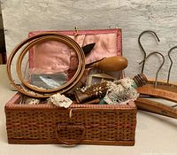 Woven sewing basket open showing pink quilted lining and vintage sewing supplies including wooden handled tool, lace trims, embroidery hoops.