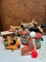 Photo showing assortment of vintage wooden toys including wooden dogs, pull toy seal, whack-a-mole game with figurines, and doll table