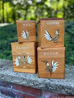 Four wooden nesting canisters labeled Tea, Coffee, Flour, Sugar each with rooster graphic, stacked in two pairs.