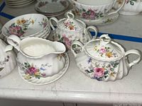 Close-up of floral patterned sugar bowls with lids and a gravy boat with matching floral design on white china.
