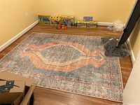 Full view of the rectangular washable area rug laid out on a wood floor, showing the multicolor pattern with central medallion and border designs in blue and coral tones.