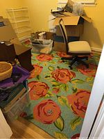 Photo showing the floral patterned area rug in a room with various items and office chair on it.