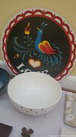 Photo showing white ceramic bowl with red dots alongside the decorative metal tray with colorful bird artwork