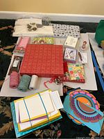 Wide shot showing all items arranged on carpet, including twine spools, a large red box, wrapped stationery packs, and assorted sheets of paper.