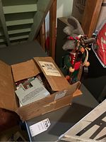 Nutcracker figure standing next to cardboard box containing wood buildings.