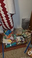 Photo showing patchwork quilt, fabric scraps, and containers with sewing supplies in a basement setting.