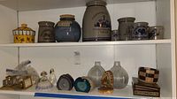 Overall shelf view with ceramic jars, glass vases, figurines, geode crystals, and small wooden box