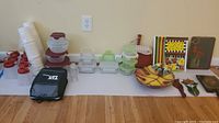 Wide view showing entire lot lineup including plastic containers, paper cups, glass containers, carrying bag, serving bowl, baskets, stained glass and plaques.