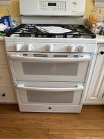Front view of white GE freestanding gas range installed between cabinets